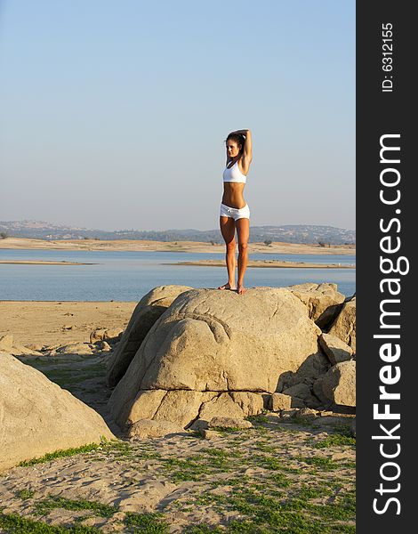 A young woman on top of a rock doing yoga at sunset in a white fitness outfit