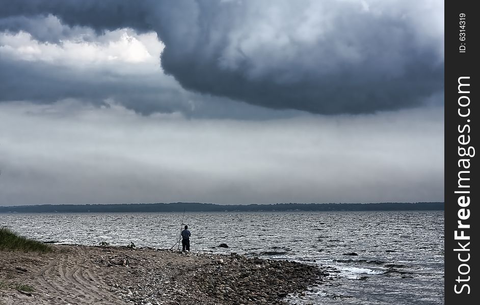 View of lone fisherman on the sound with distant storm clouds.
