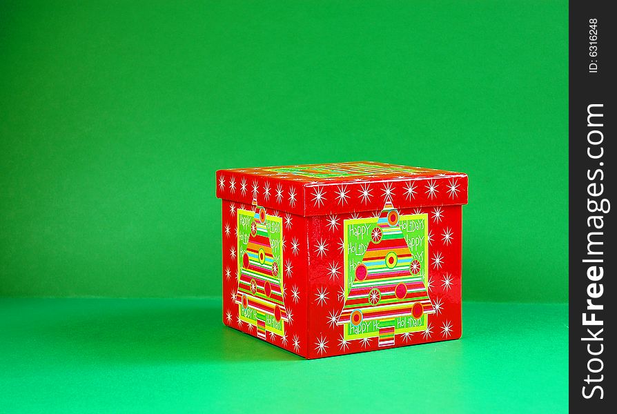 A red decorated box of a Christmas gift on a green background.