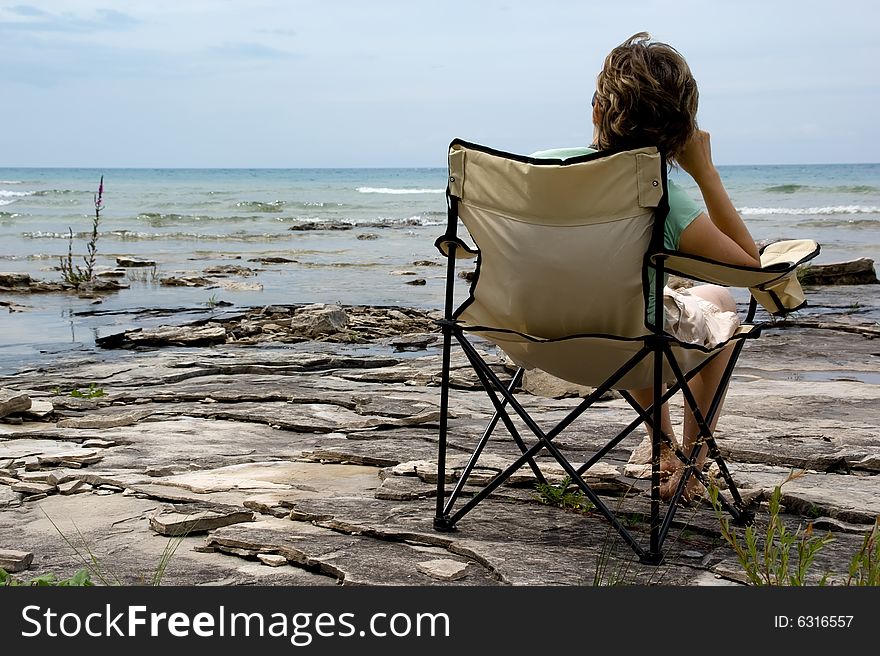 A woman resting on chair at the coastline. Huron lake, Canadian shield. Ontario, Canada. A woman resting on chair at the coastline. Huron lake, Canadian shield. Ontario, Canada.