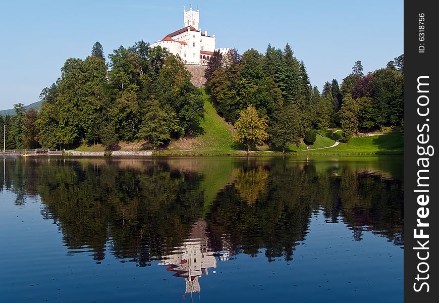 A castle on top of the hill surrounded with trees and lake