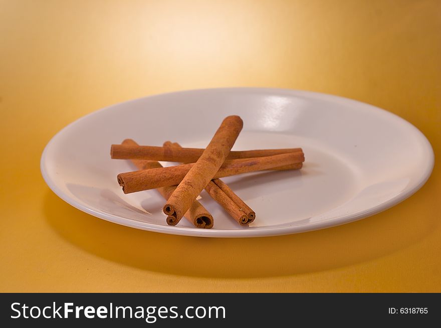 Cinnamon sticks on a white plate over a gold background