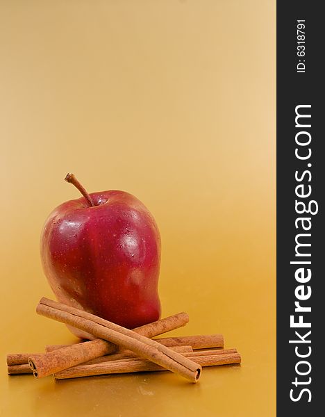 A red delicious apple with cinnamon sticks over a gold background