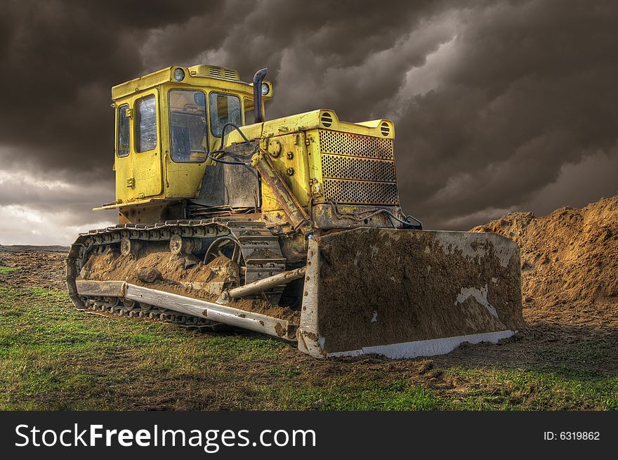 Yellow bulldozer and dark clouds in background.