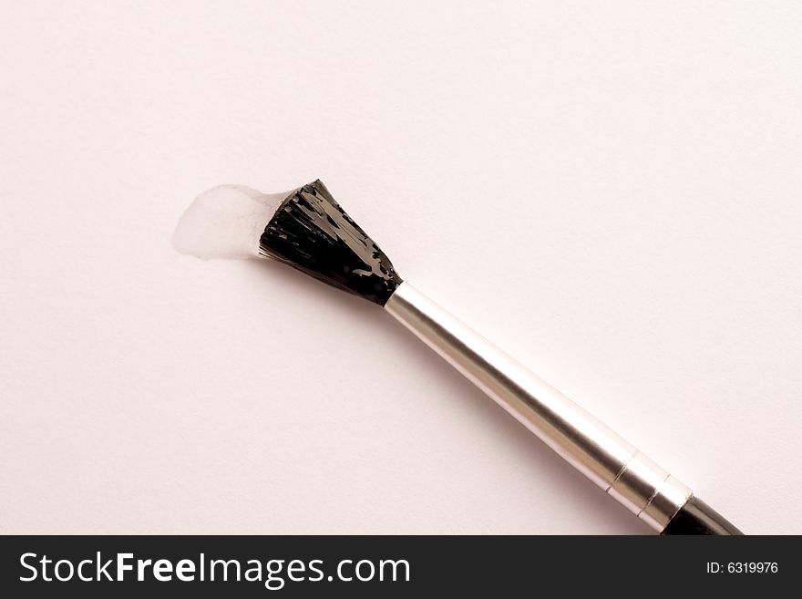 Close-up of paint brush tip covered in clear paint on white paper with black and silver handle. Close-up of paint brush tip covered in clear paint on white paper with black and silver handle