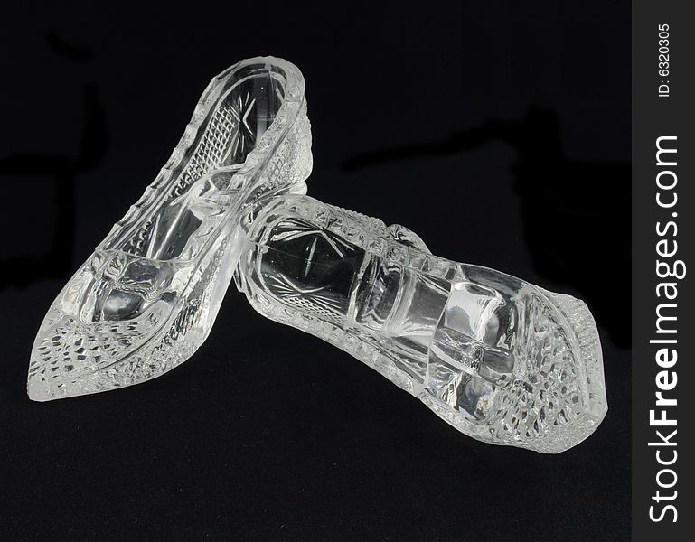 Two crystal glass slippers over black background