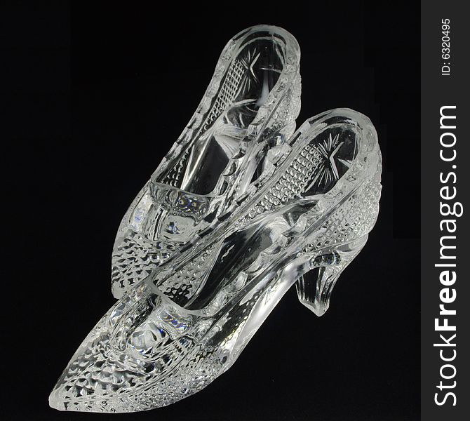 Two crystal glass slippers over black background