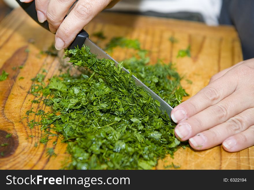 A mixture of freshly cut dill and chevril on a wooden cutting board, to be used in a gourmet meal. The hands of the chef can be seen operating the knife while cutting the herbs. A mixture of freshly cut dill and chevril on a wooden cutting board, to be used in a gourmet meal. The hands of the chef can be seen operating the knife while cutting the herbs.