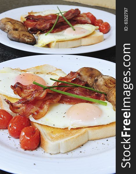 A delicious healthy gourmet breakfast with perfectly fried eggs on white toast, bacon, oven baked cherry tomatoes, fried mushrooms and garnish. A delicious healthy gourmet breakfast with perfectly fried eggs on white toast, bacon, oven baked cherry tomatoes, fried mushrooms and garnish.