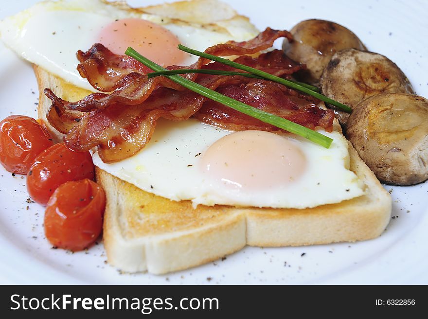 A delicious healthy gourmet breakfast with perfectly fried eggs on white toast, bacon, oven baked cherry tomatoes, fried mushrooms and garnish. A delicious healthy gourmet breakfast with perfectly fried eggs on white toast, bacon, oven baked cherry tomatoes, fried mushrooms and garnish.