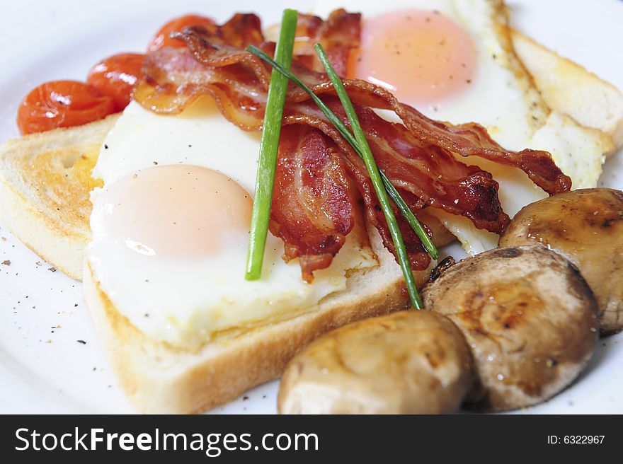 A delicious healthy gourmet breakfast with perfectly fried eggs on white toast, bacon, oven baked cherry tomatoes, fried mushrooms and garnish. A delicious healthy gourmet breakfast with perfectly fried eggs on white toast, bacon, oven baked cherry tomatoes, fried mushrooms and garnish.