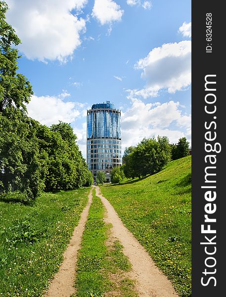 A dirt unsurfaced road contrasting with a modern-style highrise building. A dirt unsurfaced road contrasting with a modern-style highrise building