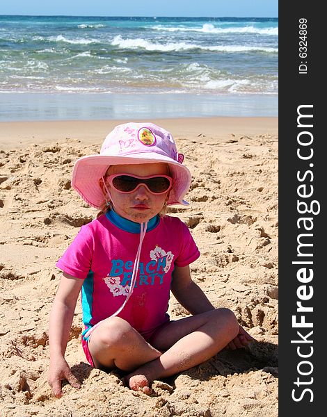 Little girl playing in the sand on the beach with a dirty face wearing a hat and sunglasses. Little girl playing in the sand on the beach with a dirty face wearing a hat and sunglasses