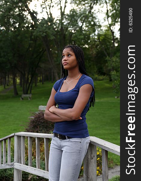 Pretty black teenage girl standing in a park and leaning on a bridge