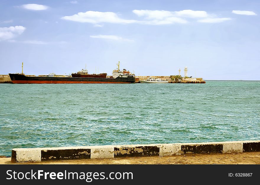 City Yalta. The peninsula of Crimea. Ukraine. Sunny day transport ship is far from the pier. Adjacent to the small boat. Even farther on the edge of the pier stands a lighthouse. City Yalta. The peninsula of Crimea. Ukraine. Sunny day transport ship is far from the pier. Adjacent to the small boat. Even farther on the edge of the pier stands a lighthouse.