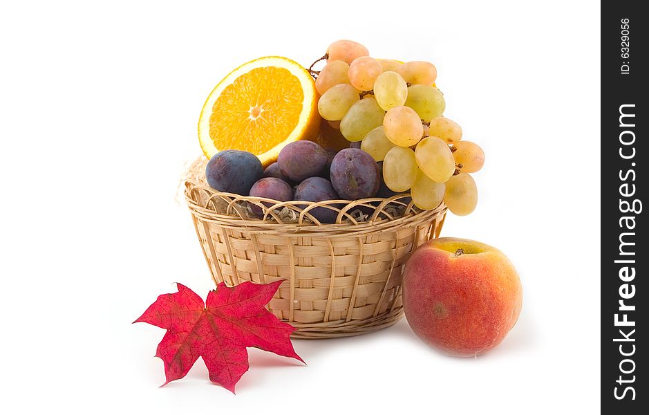 Grapes and an orange with plums in a yellow basket on a white background