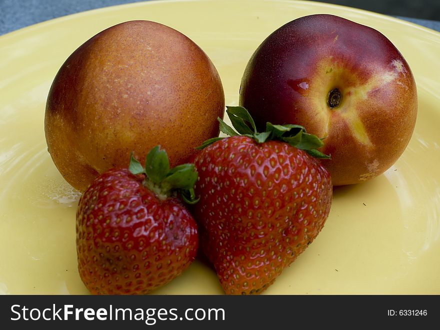 Two strawberries and two nectarines on a yellow plate. Two strawberries and two nectarines on a yellow plate