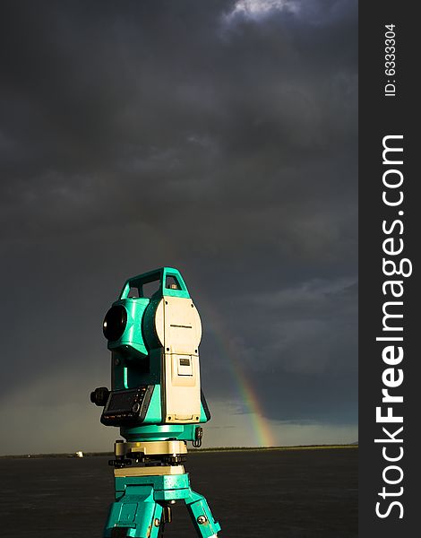 A total station in field in front of rainbow hanging over a river. A total station in field in front of rainbow hanging over a river