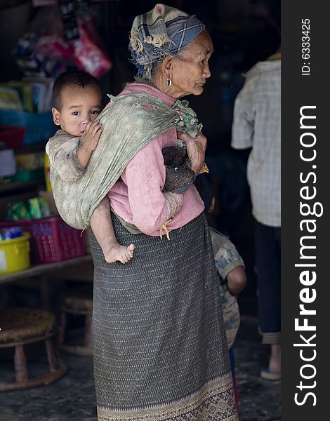 Asia, old woman with grandchild and chicken in a village of Laos