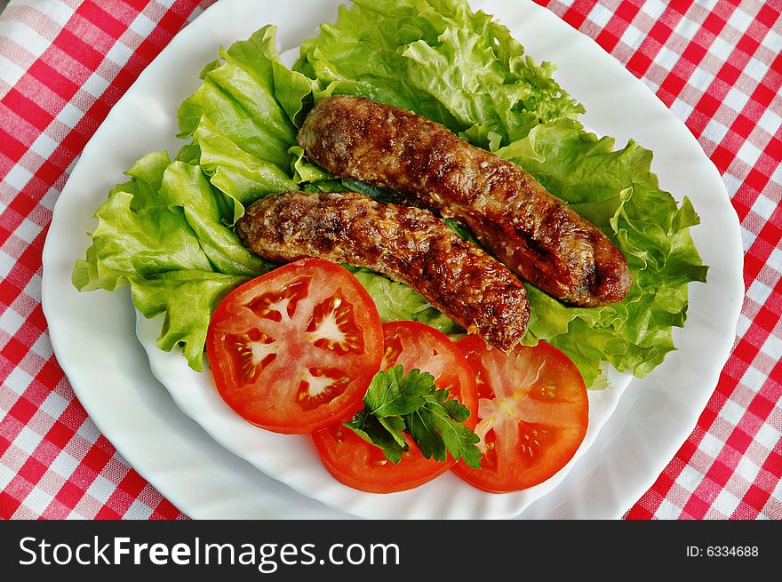 Delicious grill sausages served with salad and tomatoes in a white dish.