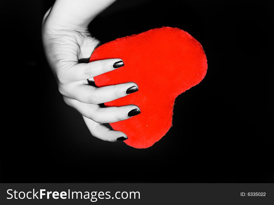 Brightly red heart in a female hand on a black background. Brightly red heart in a female hand on a black background