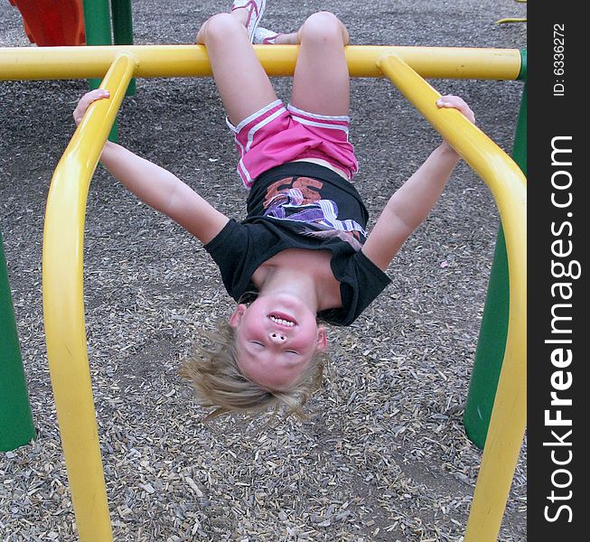 Little girl hangs upside down on the jungle gym at the playground. Little girl hangs upside down on the jungle gym at the playground.