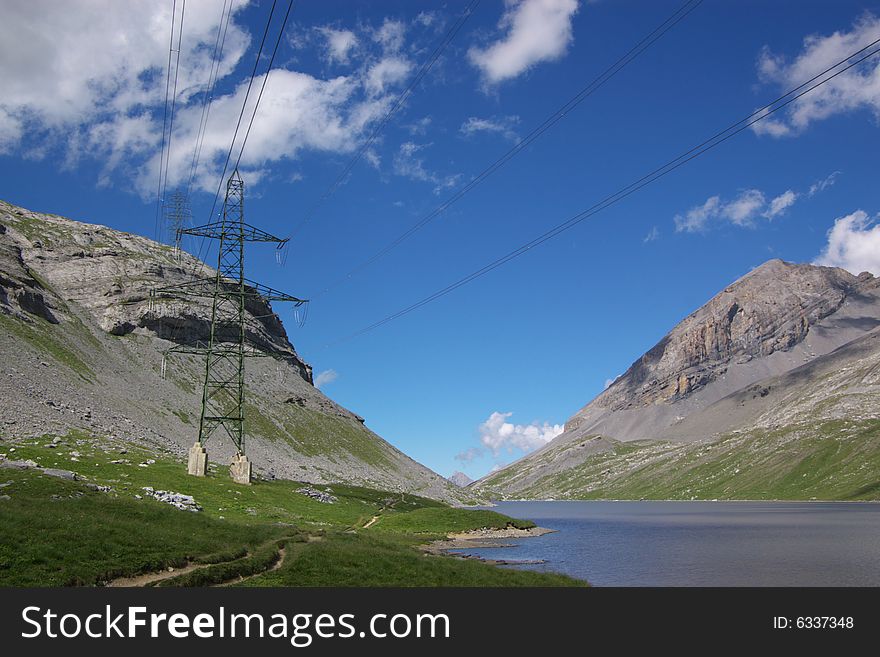 A  view on mountains lake and electricity pylon in Swiss Alps under deep blue sky, horizontal. A  view on mountains lake and electricity pylon in Swiss Alps under deep blue sky, horizontal.