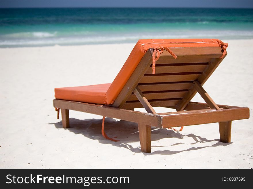 An orange bedchair facing the turquoise sea on a white sand beach. An orange bedchair facing the turquoise sea on a white sand beach