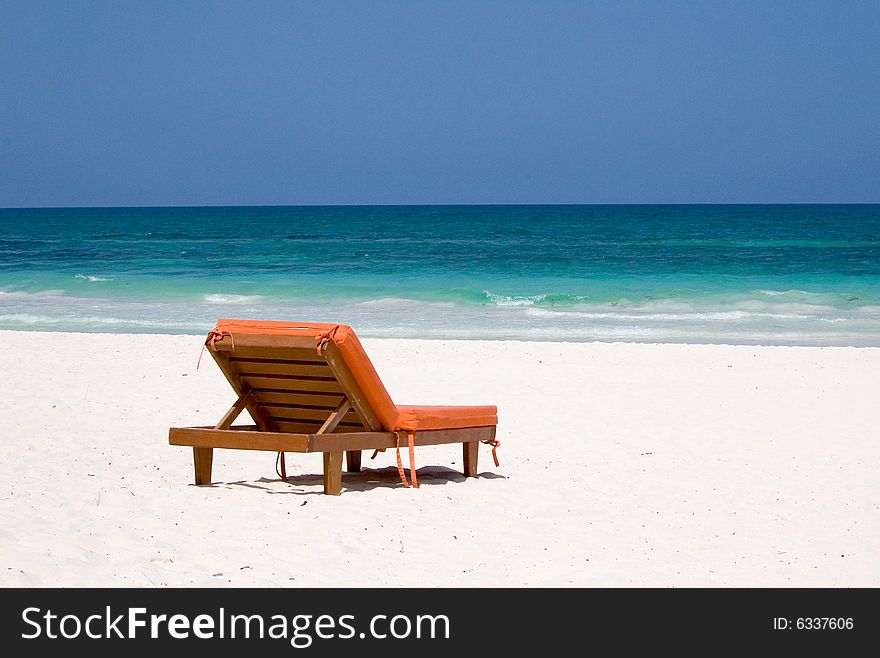 An orange bedchair facing the turquoise sea on a white sand beach in Mexico. An orange bedchair facing the turquoise sea on a white sand beach in Mexico