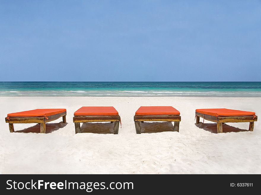 Four orange bedchairs facing the sea on a white sand beach in Mexico