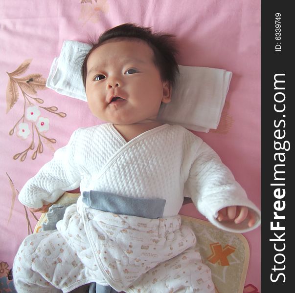 A Chinese infant is smiling on a bed. A Chinese infant is smiling on a bed