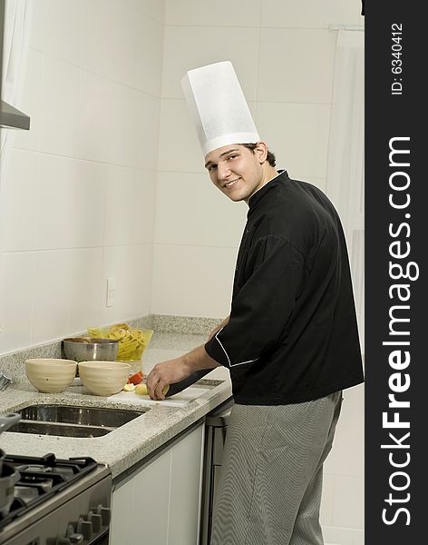 Young, smiling chef in a kitchen slicing tomatoes in a bowl. Vertically framed photo.