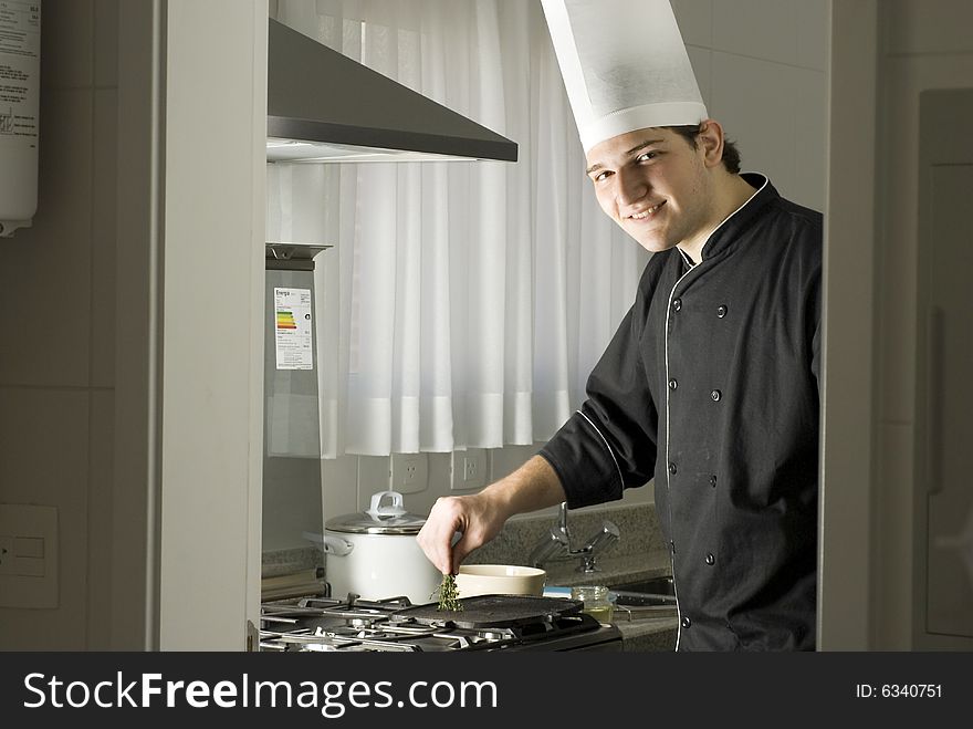 Smiling chef standing over a stove holding parsley above a griddle. Horizontally framed photo. Smiling chef standing over a stove holding parsley above a griddle. Horizontally framed photo.