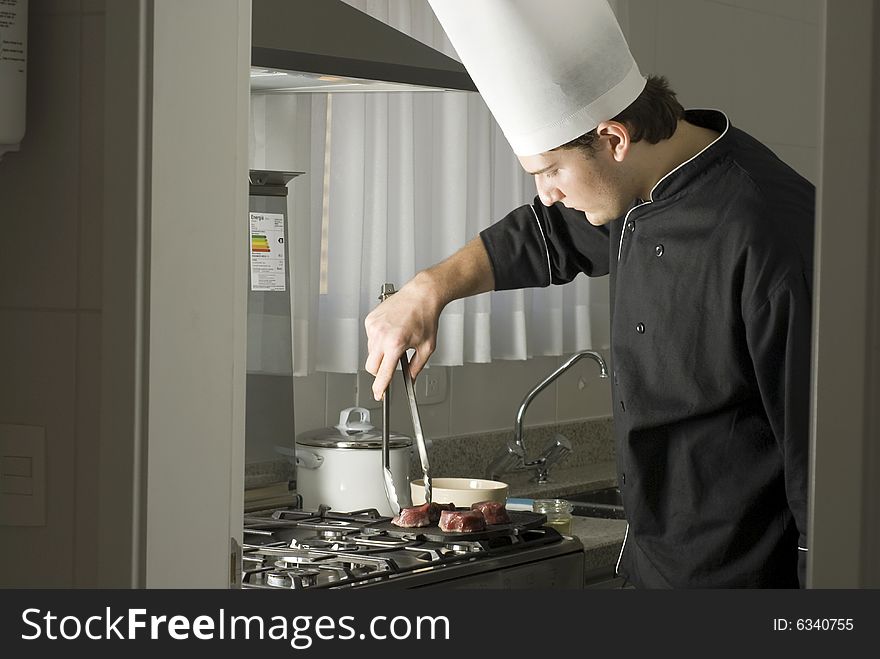 Young chef grilling steaks on a griddle on a stove in a kitchen. Horizontally framed photo.