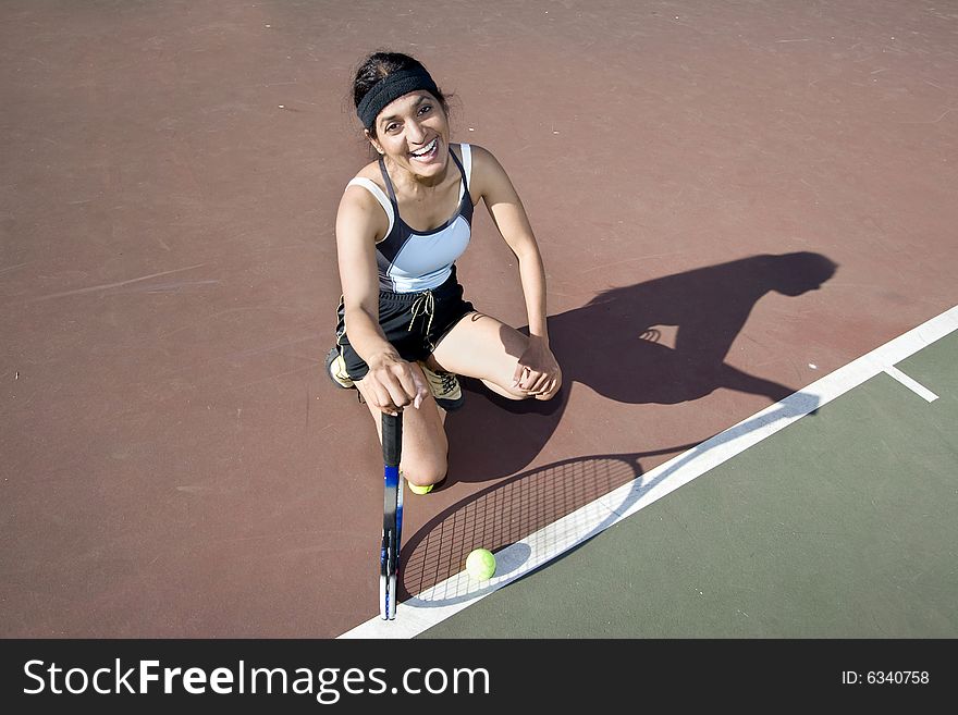 Female tennis player holding her racket crouched down on a tennis court smiling and laughing. Horizontally framed photo.
