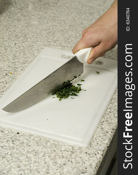 Chef's hands slicing parsley with a knife on a cutting board on a counter top. Vertically framed photo.