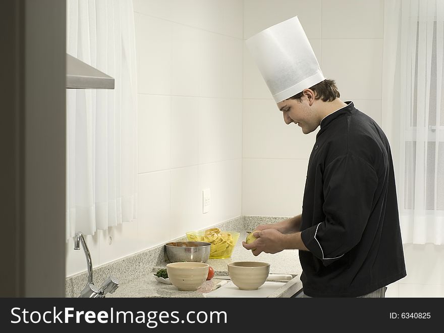 Young, smiling, chef  peeling potatoes into a bowl on a counter next to a bowl and tomatoes. Horizontally framed photo. Young, smiling, chef  peeling potatoes into a bowl on a counter next to a bowl and tomatoes. Horizontally framed photo.