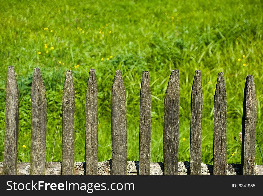 Old wooden fence and a green meadow in a village. Old wooden fence and a green meadow in a village.