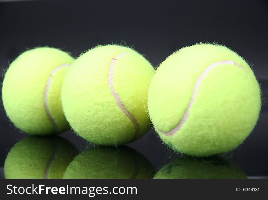 Three tennis balls with reflection over black background