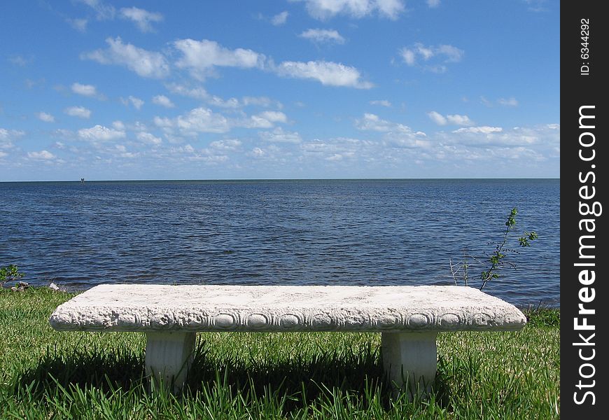 A peaceful, relaxing scene of a white bench, in the grass, by the ocean. A peaceful, relaxing scene of a white bench, in the grass, by the ocean