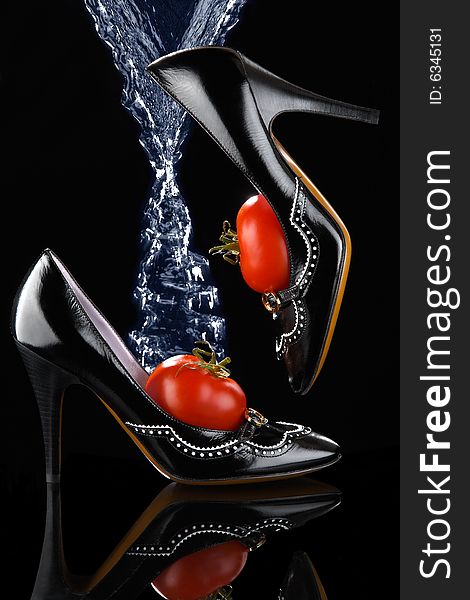 A pair of black female shoes containing tomatoes with water being poured on them. A pair of black female shoes containing tomatoes with water being poured on them.