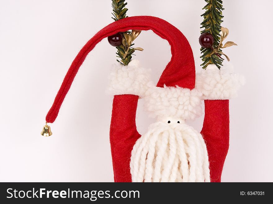 A felt and yarn folk art Santa with a bell topped red hat swings from strands of evergreen.