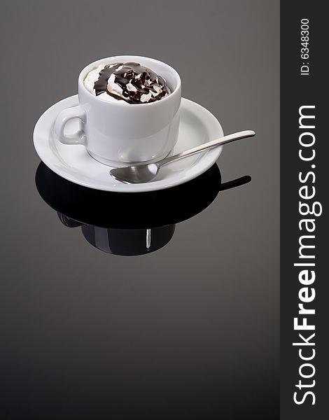 A cup of coffee on silver background with saucer, whipped cream and chocolate