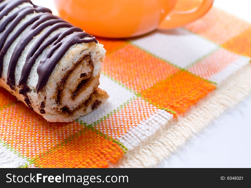 Chocolate tasty roll and orange cup on napkin. Chocolate tasty roll and orange cup on napkin