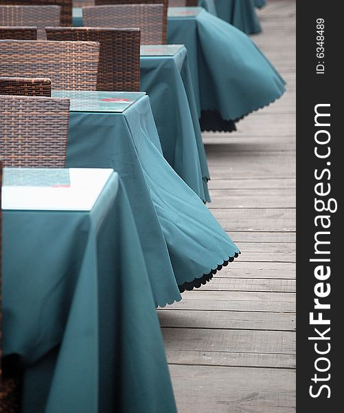 Table and chairs on wooden floor in a outdoor bar at the beach. Table clothes waving in the wind.