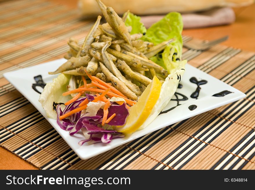 Fried fish served on plate with lemon and salad