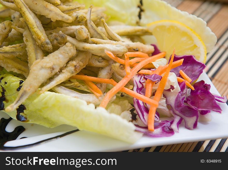 Fried fish served on plate with lemon and salad