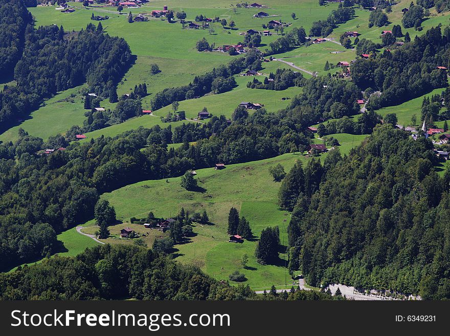 Summer rural landscape view on green Alps mountains, trees, slopes, and wooden detached houses. Alps, Switzerland, europe. Summer rural landscape view on green Alps mountains, trees, slopes, and wooden detached houses. Alps, Switzerland, europe.