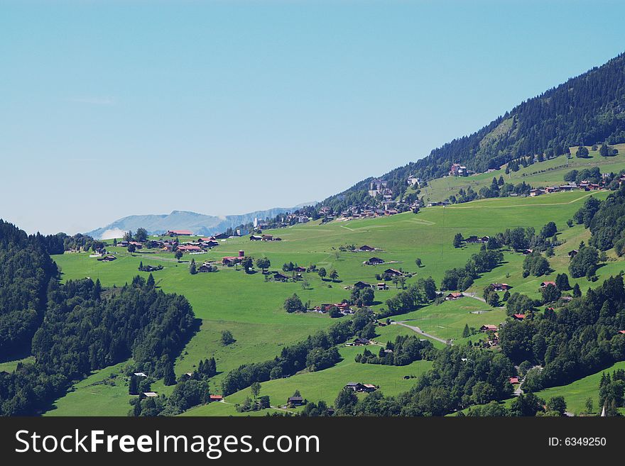 Summer rural landscape view on green Alps mountains, trees, slopes, and detached houses under clear sky. Alps, Switzerland, europe. Summer rural landscape view on green Alps mountains, trees, slopes, and detached houses under clear sky. Alps, Switzerland, europe.