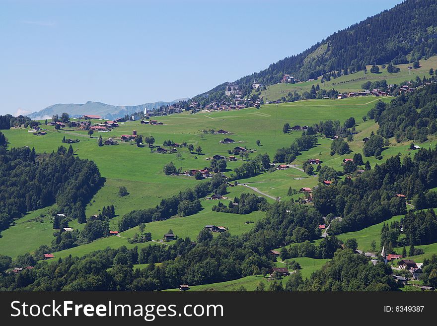 Summer rural landscape view on green Alps mountains, trees, slopes, and wooden detached houses. Alps, Switzerland, europe. Summer rural landscape view on green Alps mountains, trees, slopes, and wooden detached houses. Alps, Switzerland, europe.